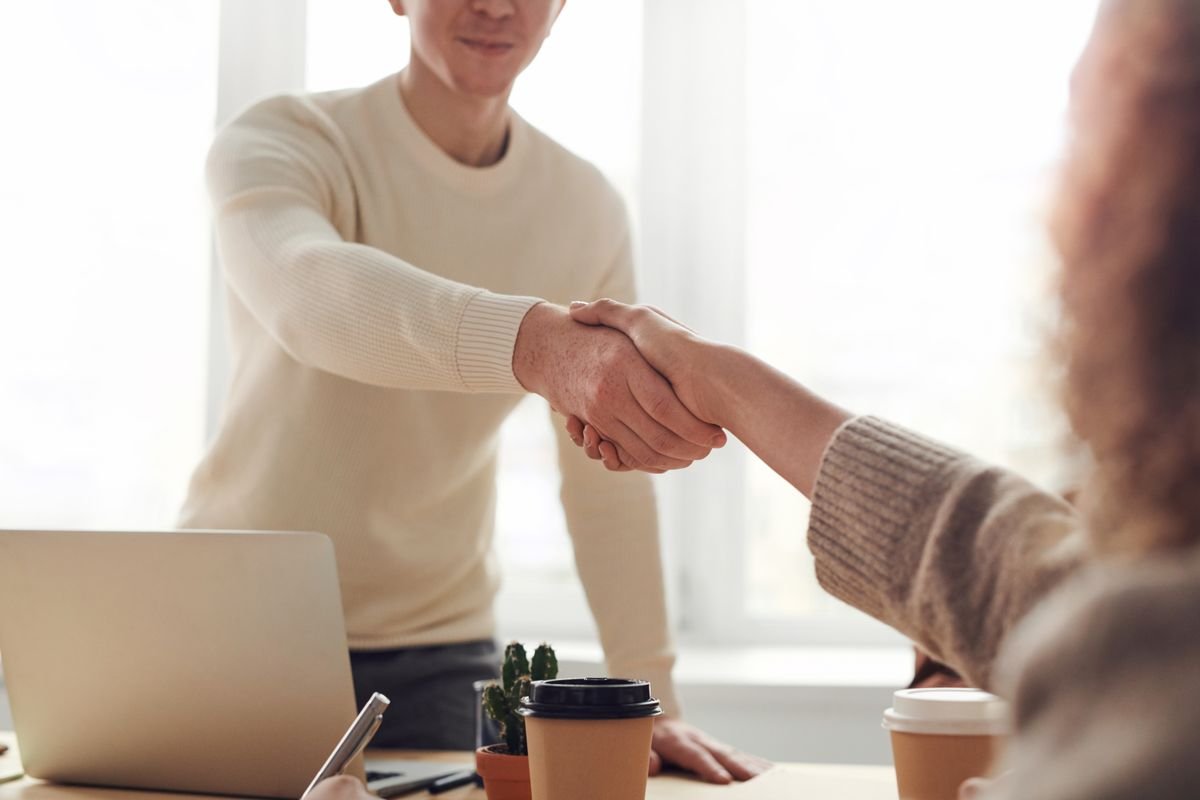 Accountant and client shaking hands across a desk with a laptop